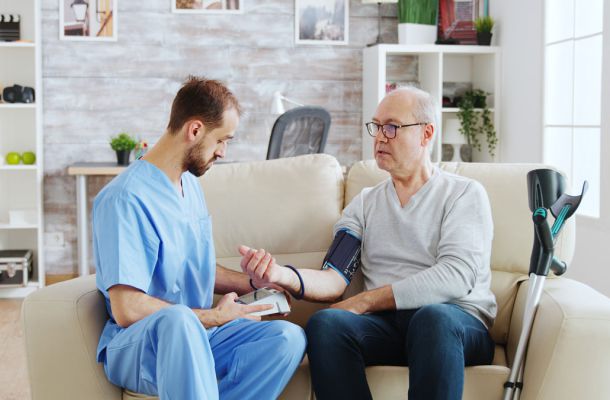 Hausbesuch: Pflegekraft misst Blutdruck bei älterem Patienten im häuslichen Umfeld, medizinische Betreuung in der Pflege