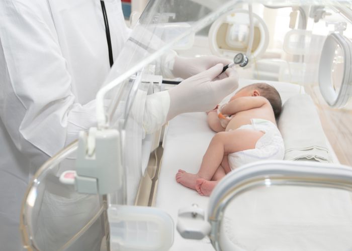 Arzt untersucht Neugeborenes im Inkubator mit Stethoskop, neonatologische Versorgung auf der Intensivstation