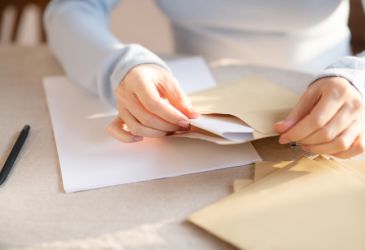 Hände öffnen einen Briefumschlag mit Dokumenten, Symbolbild für schriftliche Mitteilung im medizinischen Kontext