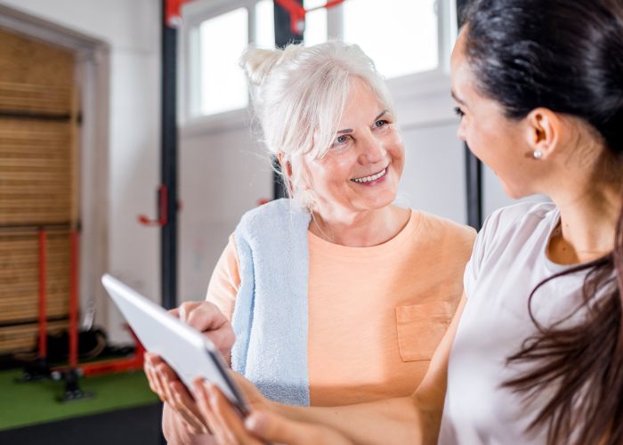 Ältere Patientin bespricht Trainingsplan mit Therapeutin in Praxis, digitale Betreuung und Rehabilitation im Gespräch