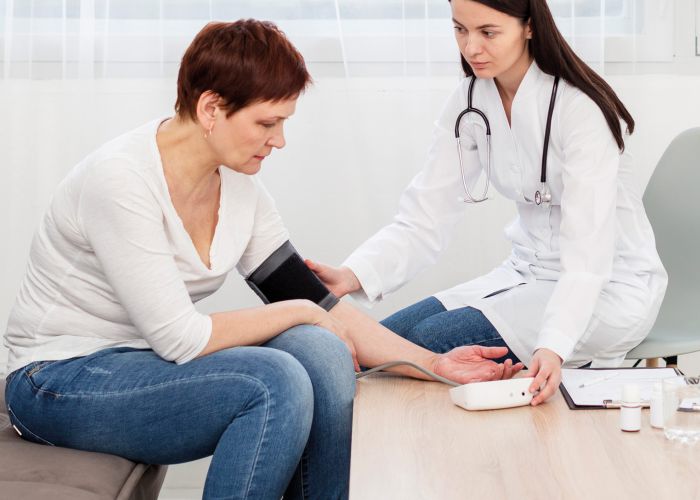 Ärztin misst Blutdruck bei Patientin im häuslichen Umfeld, medizinische Untersuchung im Rahmen eines Hausbesuchs