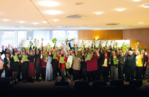 Feierliche Zeugnisübergabe: Absolventinnen und Absolventen halten Urkunden und Blumen bei Abschlussveranstaltung im Saal