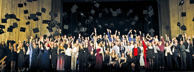 Abschlussfeier Humanmedizin: Absolventinnen und Absolventen werfen Hüte in die Luft auf der Bühne im Hörsaal