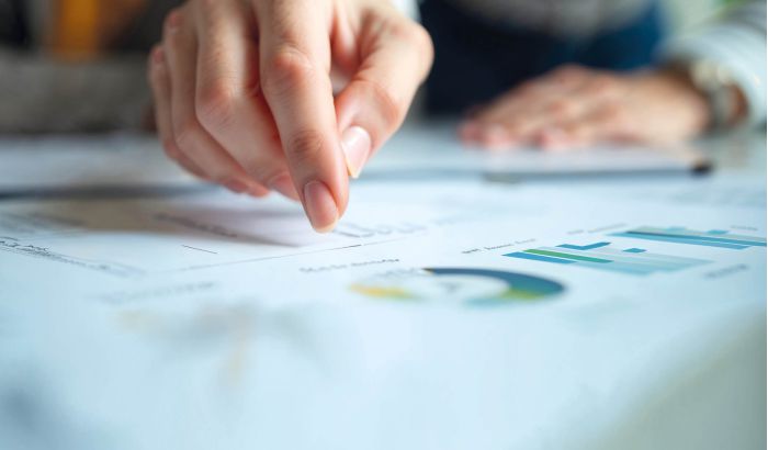 Sitzung der Ärztekammer mit zahlreichen Teilnehmern an Tischen, Vortragendem am Podium und Präsentation im Konferenzraum.