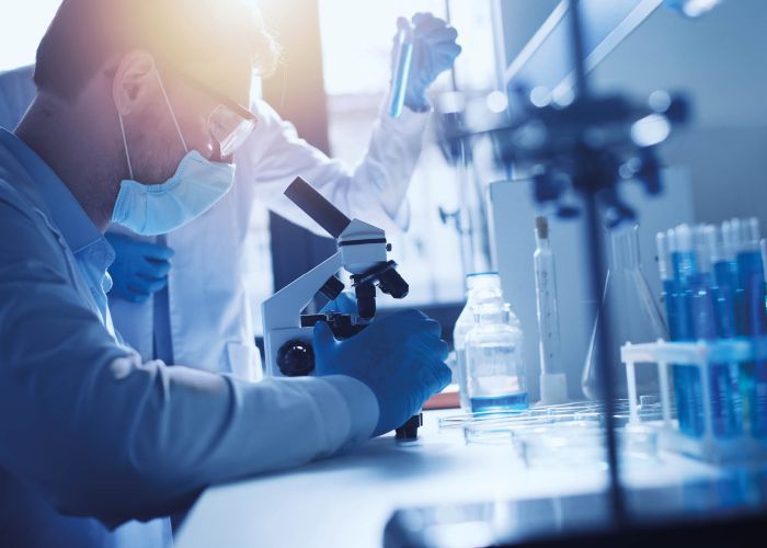 Laborforscher mit Schutzmaske arbeitet am Mikroskop, Reagenzgläser und Probenanalyse im modernen Forschungslabor