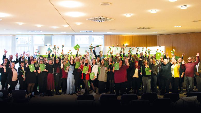 Feierliche Zeugnisübergabe: Absolventinnen und Absolventen halten Urkunden und Blumen bei Abschlussveranstaltung im Saal