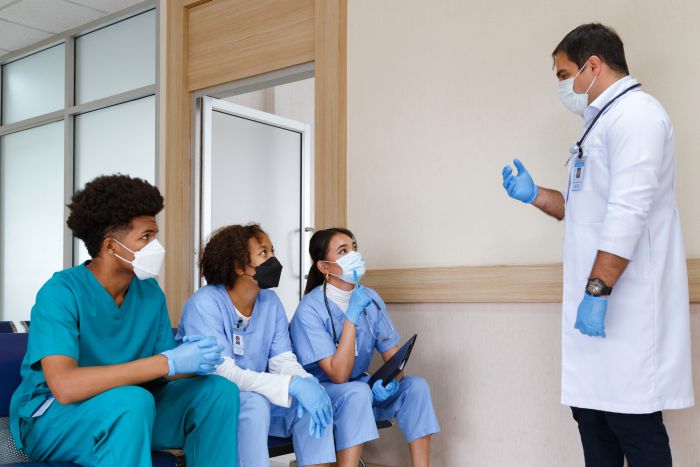 Sitzung der Ärztekammer mit zahlreichen Teilnehmern an Tischen, Vortragendem am Podium und Präsentation im Konferenzraum.