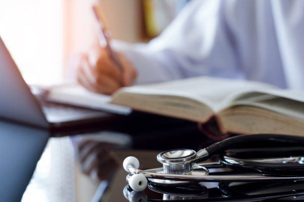 Arzt mit Stethoskop bei medizinischer Fortbildung, schreibt Notizen zu Fachliteratur für Weiterbildung und Praxiswissen.