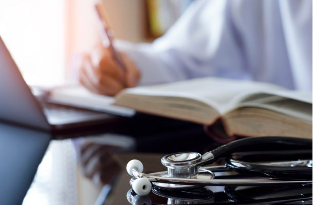 Arzt mit Stethoskop bei medizinischer Fortbildung, schreibt Notizen zu Fachliteratur für Weiterbildung und Praxiswissen.