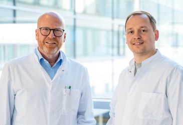 Zwei Ärzte in weißen Kitteln in heller Klinik vor Fensterfront