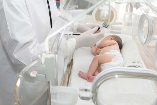 Neugeborenes im Inkubator wird von einem Arzt mit Stethoskop untersucht; medizinische Versorgung auf der Neonatologie.