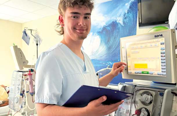 Pflegekraft bedient Dialysegerät und hält Klemmbrett – medizinische Tätigkeit in einer modernen Klinikumgebung.