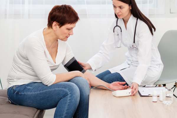 Ärztin misst einer sitzenden Patientin den Blutdruck mit einer automatischen Manschette in einer Praxisumgebung.