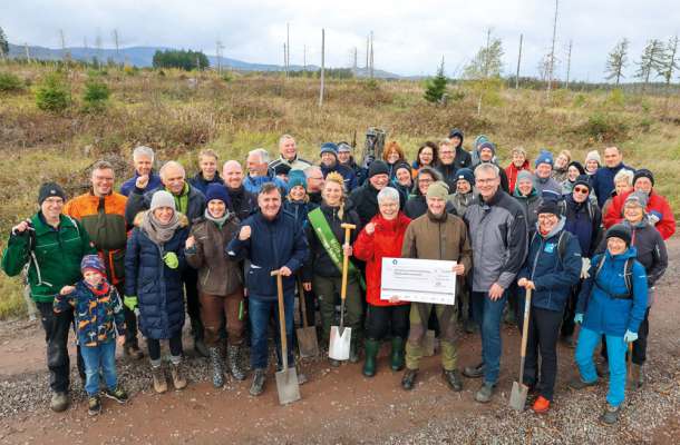 Große Gruppe von Teilnehmenden bei einer Baumpflanzaktion im Harz, einige mit Spaten und einem Spendenscheck.