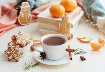 Tasse Tee mit Zimtstangen, Mandarinen und Weihnachtsgebäck in gemütlicher Adventsstimmung auf festlich gedecktem Tisch.