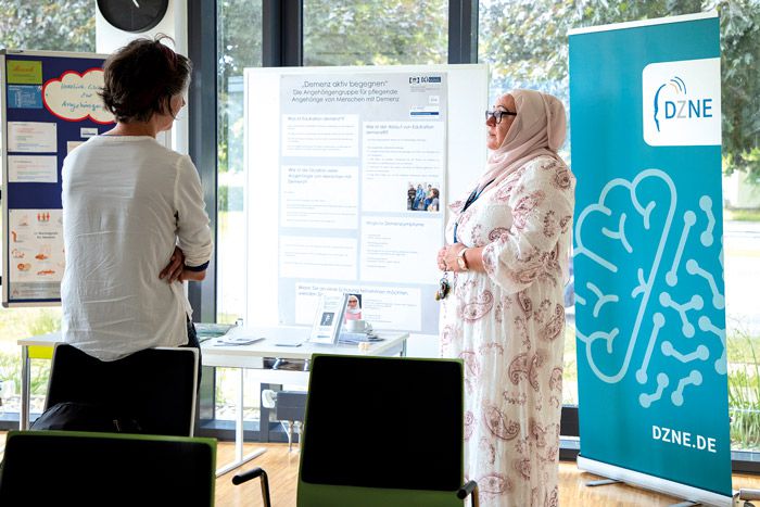 Infostand des DZNE beim Ethiktag mit Beratung zu Demenz, Austausch zwischen Fachperson und Besucher im Veranstaltungsraum.