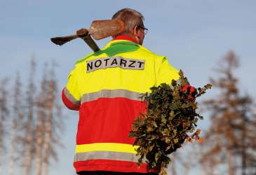 Notarzt bei Pflanzaktion mit Schaufel und Baumsetzlingen zur Unterstützung von Umwelt- und Gesundheitsprojekten.