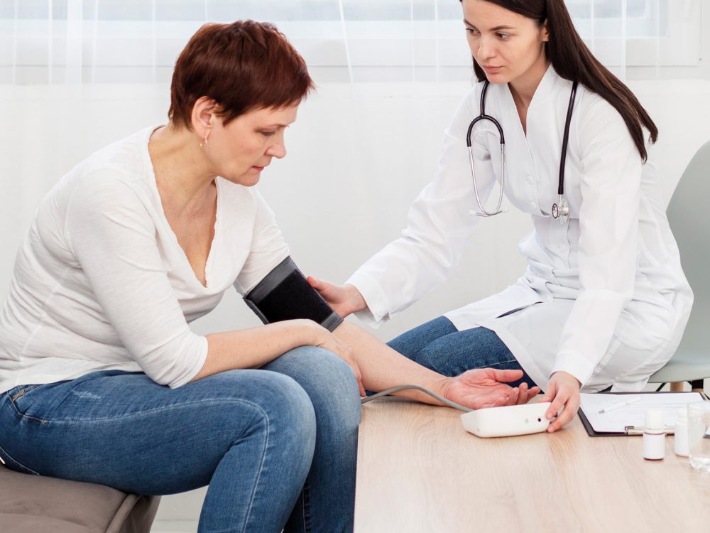 Ärztin misst Blutdruck einer Patientin im Gespräch – medizinische Untersuchung in moderner Praxisumgebung.