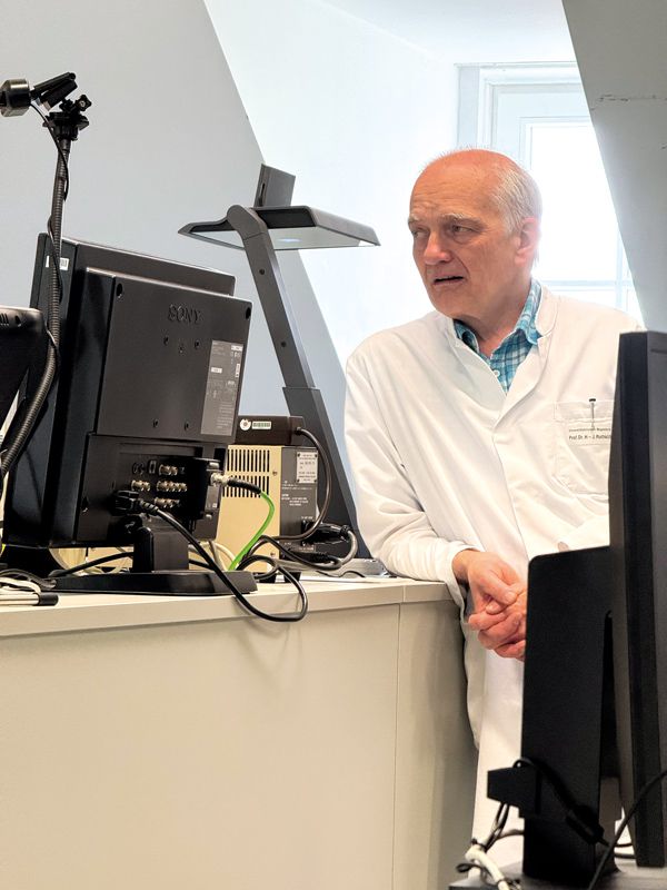 Medizinprofessor im weißen Kittel erklärt Inhalte am Computer während einer Lehrveranstaltung für Studierende.