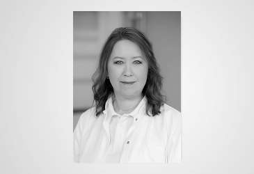 Schwarzweiß-Porträt einer medizinischen Fachkraft in Arbeitskleidung, sachliche Darstellung im klinischen Umfeld.