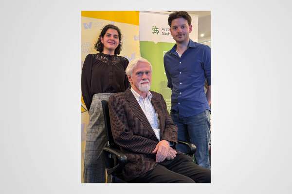 Drei Personen bei einer Veranstaltung der Ärztekammer Sachsen-Anhalt, ein älterer Mann sitzend, zwei junge Erwachsene stehend.