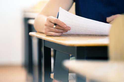 Schriftliche Prüfung im medizinischen Kontext: Hand mit Stift bearbeitet Prüfungsunterlagen an einem Schreibtisch.