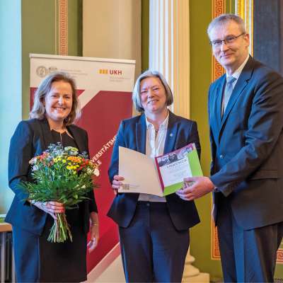 Ehrung bei medizinischer Veranstaltung: Urkundenübergabe und Blumen an eine Wissenschaftlerin im festlichen Rahmen.