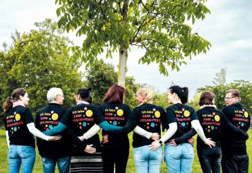 Gruppe von Organempfängern mit Shirts „Ich lebe dank Organspende“ steht vereint unter einem Baum im Park.