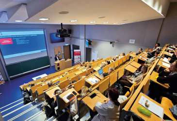 Vortrag in einem großen Hörsaal mit zahlreichen Teilnehmern, die einer medizinischen Präsentation aufmerksam folgen.