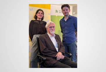 Drei Personen bei einer Veranstaltung der Ärztekammer Sachsen-Anhalt, ein älterer Mann sitzend, zwei junge Erwachsene stehend.