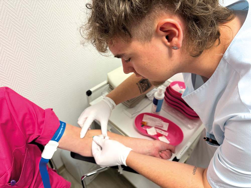 Medizinische Fachkraft entnimmt Blutprobe bei Patientin – hygienisches Arbeiten im Labor oder Behandlungsraum.