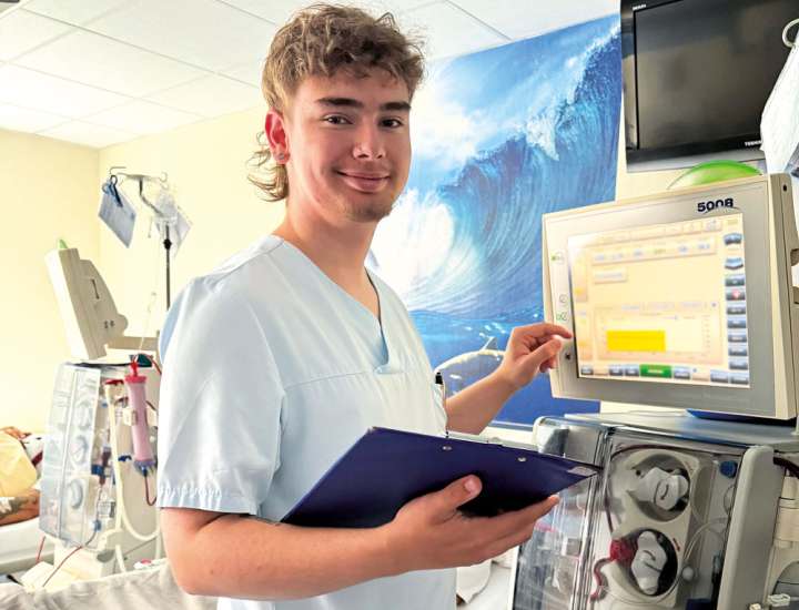 Pflegekraft bedient Dialysegerät und hält Klemmbrett – medizinische Tätigkeit in einer modernen Klinikumgebung.