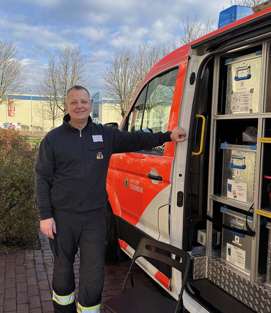 Feuerwehrangehöriger steht an geöffnetem Einsatzfahrzeug mit medizinischer Ausrüstung und Materialboxen für den Rettungseinsatz.