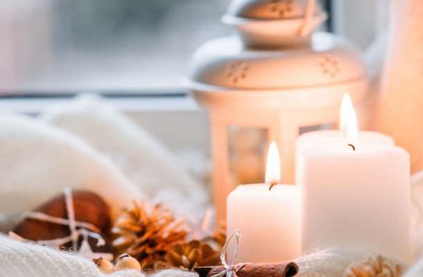 Adventsvorbereitungen mit brennenden Kerzen, Zimtstangen und Laterne als Symbol für Besinnung in der Weihnachtszeit.