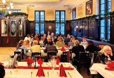Festlich geschmückter Gastraum mit langen Tischen, zahlreichen Gästen und weihnachtlicher Dekoration bei geselligem Beisammensein.