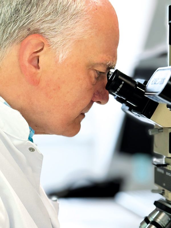 Medizinprofessor betrachtet eine Probe durch ein Mikroskop während eines Seminars zur Differentialdiagnose.