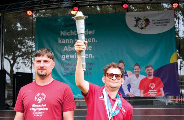 Athlet hält die Fackel der Special Olympics Landesspiele Sachsen-Anhalt 2025 auf der Bühne in Halle hoch.
