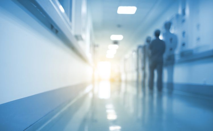 Unschärfeaufnahme eines Krankenhausflurs mit medizinischem Personal, das in der Ferne in Richtung Lichtquelle geht.