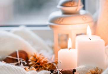 Adventsvorbereitungen mit brennenden Kerzen, Zimtstangen und Laterne als Symbol für Besinnung in der Weihnachtszeit.