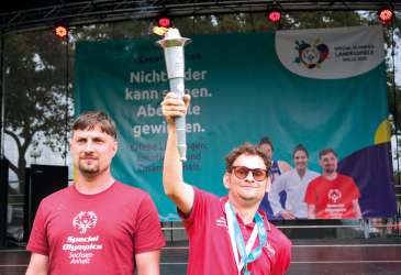 Athlet hält die Fackel der Special Olympics Landesspiele Sachsen-Anhalt 2025 auf der Bühne in Halle hoch.