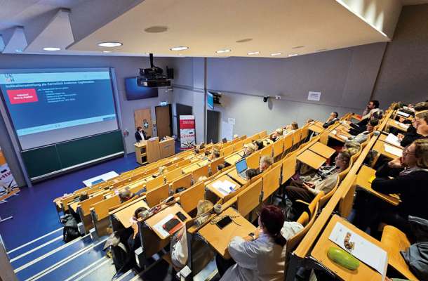 Vortrag in einem großen Hörsaal mit zahlreichen Teilnehmern, die einer medizinischen Präsentation aufmerksam folgen.