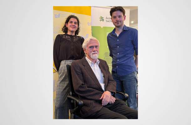 Drei Personen bei einer Veranstaltung der Ärztekammer Sachsen-Anhalt, ein älterer Mann sitzend, zwei junge Erwachsene stehend.