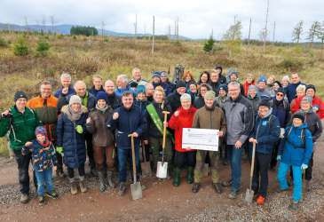 Große Gruppe von Teilnehmenden bei einer Baumpflanzaktion im Harz, einige mit Spaten und einem Spendenscheck.