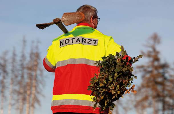 Notarzt bei Pflanzaktion mit Schaufel und Baumsetzlingen zur Unterstützung von Umwelt- und Gesundheitsprojekten.
