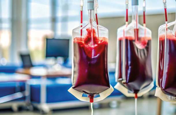 Mehrere Blutkonserven hängen an Infusionsständern in einem klinischen Behandlungsraum zur medizinischen Versorgung.